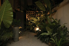 A pathway flanked by large potted plants leading to a building with a grid-like structure. - Ino Plaza Cocody (Abidjan)