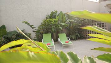 Two green lounge chairs with red cushions, a concrete floor, and various green plants.