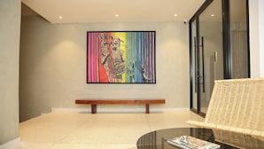 Un interior moderno con un banco, una mesa de vidrio y un cuadro abstracto y colorido en la pared.