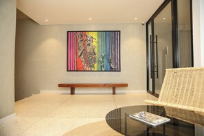A modern interior with a bench, a glass table, and a colorful abstract painting on the wall. - Ino Plaza Cocody (Abidjan)