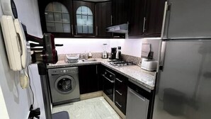 Een kleine keuken met donkere kastjes, een roestvrijstalen koelkast, een wasmachine en een magnetron.