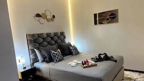 Een moderne slaapkamer met een gestoffeerd hoofdbord, een nachtkastje met lamp en een dienblad met toiletartikelen op het bed.