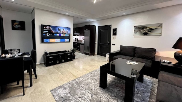 Een moderne woonkamer met een flatscreen televisie, een eethoek en een keuken op de achtergrond.