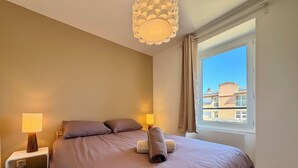 Una camera da letto con un letto, comodini, una lampada, un asciugamano e una finestra vista edifici.
