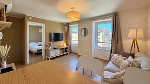 Un appartamento moderno con zona pranzo, soggiorno con divano e lampada, televisione e camera da letto con letto.