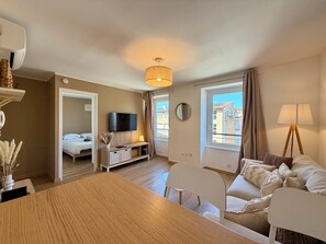 Eine moderne Wohnung mit Essbereich, einem Wohnzimmer mit Sofa und Lampe, einem Fernseher und einem Schlafzimmer mit Bett.