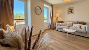 Ein Wohnzimmer mit einer Couch, einem kleinen runden Tisch, einer Lampe und Blick auf einen Berg durch das Fenster.