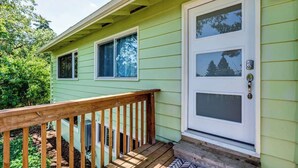 A green house with a white front door, a wooden deck, and a small porch. - Spacious 3BR • 10 Min to Autzen • Family Friendly (Eugene)