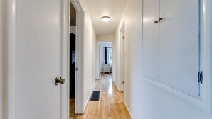 A hallway with white doors, a vent on the floor, and a view into a room with a window and curtains. - Spacious 3BR • 10 Min to Autzen • Family Friendly (Eugene)