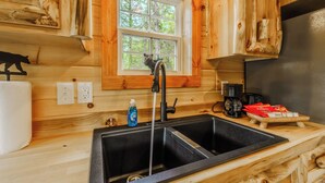 Una cocina con paredes de madera, un lavamanos doble, una ventana con vista a árboles y una cafetera sobre la encimera.