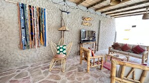 A rustic room with stone flooring, a woven chair, a sofa, a television, and a wall with hanging decorative items. - House with pool in Mancora, ideal for families. (Máncora)