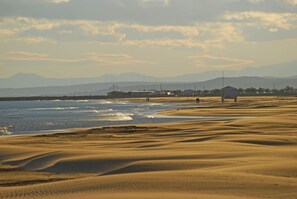 Une plage avec des dunes de sable, une étendue d’eau et des montagnes à l’horizon.