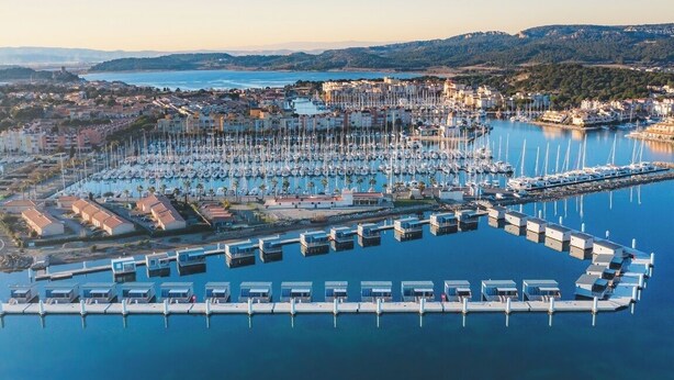 An aerial view of a marina with numerous boats docked, surrounded by residential buildings and a hilly landscape in the background. - Appartement T2 en résidence - Gruissan, France 2 travellers. (Gruissan)
