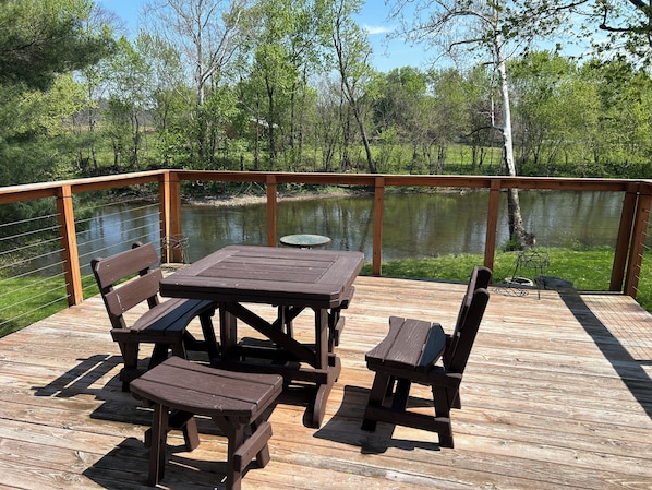 A wooden deck with a table and benches overlooking a calm lake, surrounded by trees.