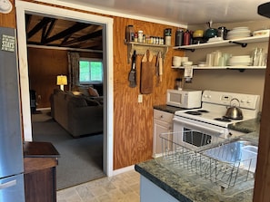 A compact kitchen with a microwave, stove, and dish rack. A wooden wall and a window are visible in the background.