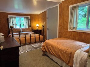 A bedroom with two beds, a bedside table, a lamp, and a window with curtains.