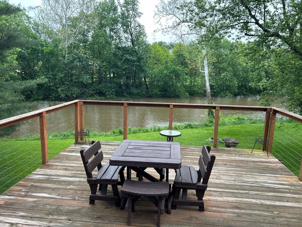 Une terrasse en bois, agrémentée d’une table et de chaises, entourée d’une balustrade en bois, et offrant une vue sur une étendue d’eau et la verdure environnante.