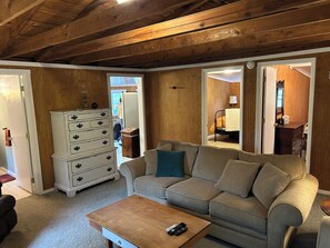 Un salon chaleureux avec un plafond en bois, un canapé beige, une commode blanche et une table basse en bois.