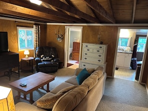 A cozy living room with a sofa, a wooden coffee table, a leather armchair, and a television.
