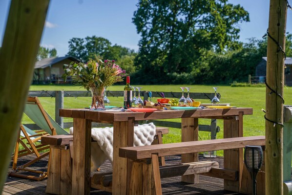 A wooden picnic table with a bottle of wine, a vase of flowers, and various food items.