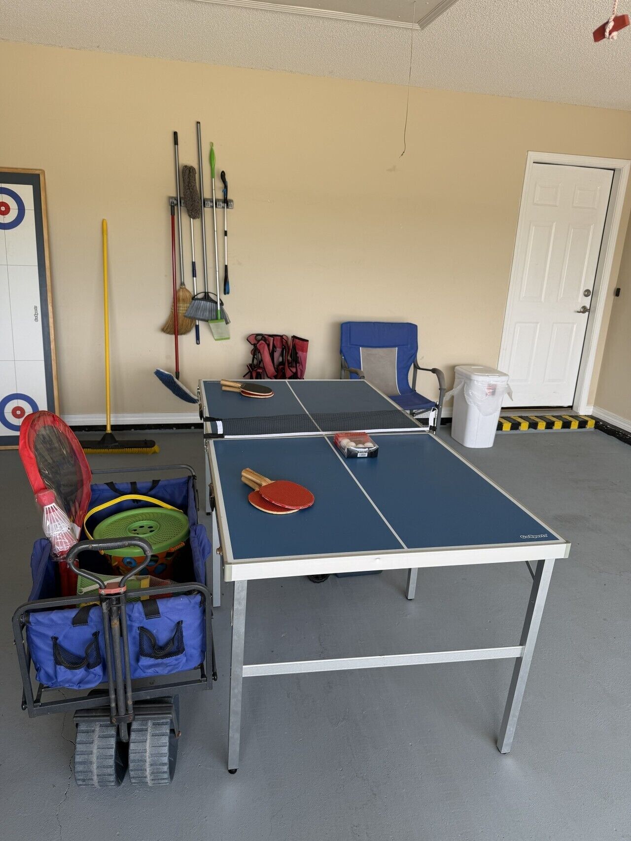 Een tafeltennistafel in een kamer met een deur, een blauwe stoel en een moprek.