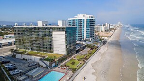 A modern hotel with a pool, beachfront view, and multiple high-rise buildings in the background. - Oceanside Inn 606 (Daytona Beach Shores)