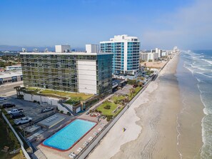 A modern hotel with a pool, beachfront view, and multiple high-rise buildings in the background. - Oceanside Inn 606 (Daytona Beach Shores)