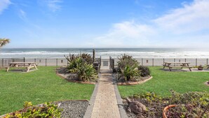 A pathway leading to a beachside patio with picnic tables and a view of the ocean. - Oceanside Inn 606 (Daytona Beach Shores)