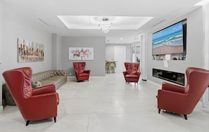 Ein modernes Wohnzimmer mit einem großen Flachbildfernseher, zwei roten Ledersesseln, einem beige farbenen Sofa und Kunstwerken an den Wänden.