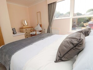 A bedroom with a bed, a dresser, a mirror, and a window with a view of the outside. - Camellia Cottage (Wimborne)