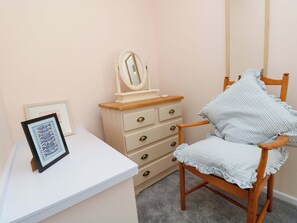 Ein Schlafzimmer mit einem weißen Schminktisch, einem Holzsessel mit gestreifter Sitzkissen, einem gerahmten Bild und einem Spiegel auf dem Schminktisch.