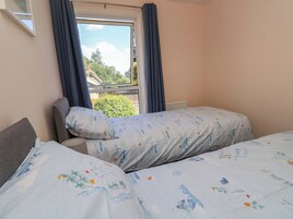 Un dormitorio con dos camas, una ventana con cortinas y vistas al verdor exterior.