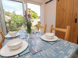 Una mesa de comedor preparada con cuencos blancos, copas de vino y un florero con flores, con vista a follaje exterior.