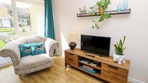 Una sala de estar con sofá, televisor, aparador de madera y una ventana con cortinas.