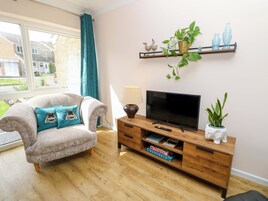 Una sala de estar con sofá, televisor, aparador de madera y una ventana con cortinas.