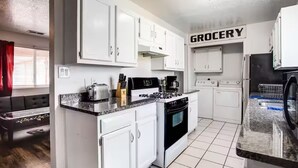 Una cucina compatta con mobili bianchi, un fornello a gas, una macchina da caffè e un frigorifero.