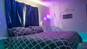 Una camera da letto con un letto, tende, una sedia sospesa e un neon.