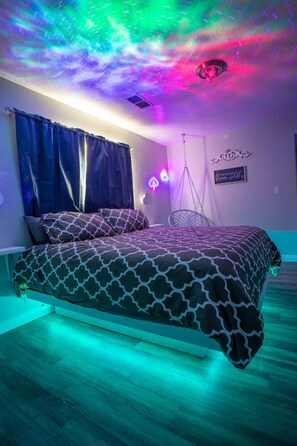 Un dormitorio con cama, cortinas, una silla colgante y un letrero de neón.