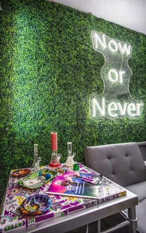 Una habitación con una pared verde y un letrero de neón que dice 'Now or Never'.