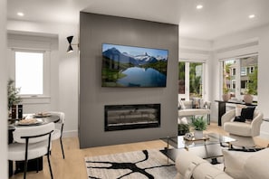 A modern living room with a flat-screen TV mounted on a wall, a fireplace below, and a dining area with a table and chairs. - Fremont Luxe Residences #2 | 2 Bedrooms, Sleeps 6 (Seattle)