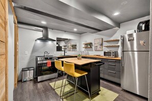 A modern kitchen with a central island, stainless steel appliances, and yellow chairs. - Deluxe West Seattle Apartment | Sleeps 6 | FIFA (Seattle)