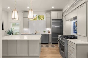 A modern kitchen with a large island, stainless steel appliances, and pendant lighting. - Luxury Alki Beach Villa | Sleeps 10 | 360° Rooftop (Seattle)