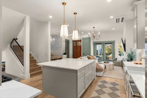 A modern kitchen with a central island, pendant lighting, and a staircase. - Luxury Alki Beach Villa | Sleeps 10 | 360° Rooftop (Seattle)
