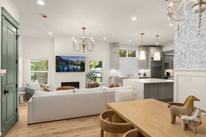 A modern kitchen with a dining area, a fireplace, and a large window overlooking a scenic landscape. - Luxury Alki Beach Villa | Sleeps 10 | 360° Rooftop (Seattle)