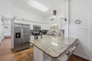 A modern kitchen with white cabinetry, stainless steel appliances, granite countertops, and pendant lighting. - Pirates Bay 3BR Getaway w/ Lagoon-Style Pool (Port Aransas)