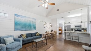 Un'ampia zona giorno con un grande quadro, una ventola a soffitto, un tavolo da pranzo e un angolo cucina con elettrodomestici moderni.