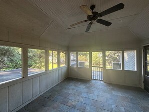 Ein Zimmer mit Deckenventilator, großen Fenstern und Blick ins Freie.