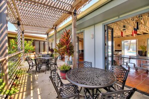 A covered outdoor patio with tables and chairs, potted plants, and a view into the interior. - Coastal Studio with Pool and Beach Boardwalk (Port Aransas)