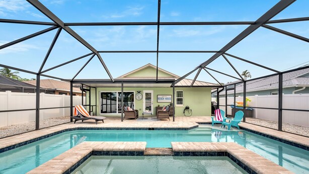 A pool area with a covered structure, lounge chairs, and a sign indicating a beach house. - Heated Pool & Hot Tub, Walk to Beach, Fully Equipped. Free Bikes. Grill. (Naples)