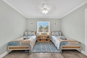 A bedroom with two beds, a window with blinds, a ceiling fan, and a bedside table with a lamp. - Heated Pool & Hot Tub, Walk to Beach, Fully Equipped. Free Bikes. Grill. (Naples)
